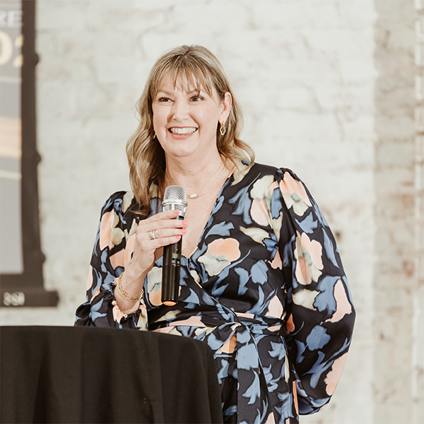 Kelly MaGee holding a microphone speaking at an event